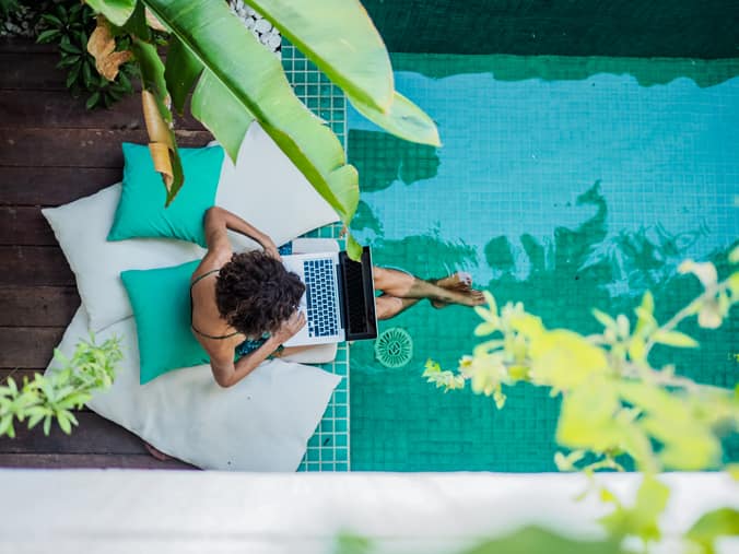 overhead photo of woman working on laptop besides pool